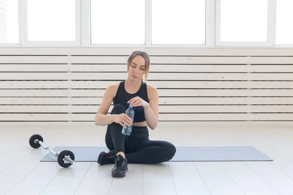 Concepto de personas, deporte y fitness: mujer joven sentada con una botella de agua en la colchoneta del gimnasio — Foto de Stock