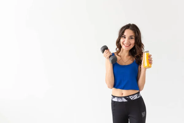 Sport, stile di vita sano, concetto di persone - giovane donna con un manubrio in mano e una bottiglia di succo in un'altra mano su sfondo bianco con spazio per copiare — Foto Stock