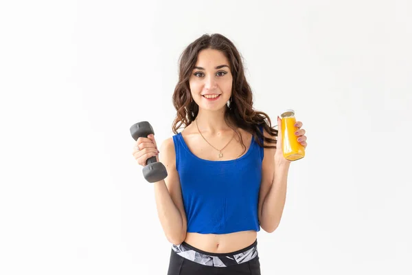 Esporte, estilo de vida saudável, conceito de pessoas - close-up de jovem com um haltere na mão e uma garrafa de suco em outra mão no fundo branco — Fotografia de Stock