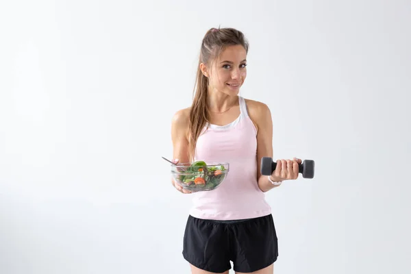 Stile di vita sano, concetto di gente - un piatto d'insalata in una mano e manubrio in un'altra mano. Sorriso e tuta fitness — Foto Stock