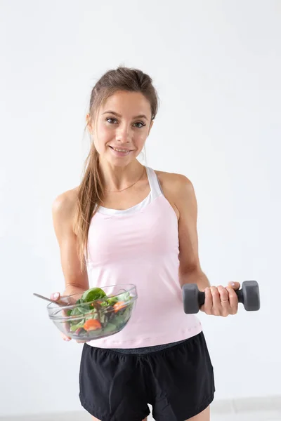 El modo de vida sano, el concepto de la gente - el plato de la ensalada en una mano y la pesa en otra mano. Sonrisa y traje de fitness — Foto de Stock