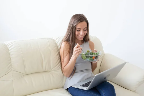 Mode de vie sain, bonne alimentation, se détendre et les gens concept- jeune belle femme assise sur le canapé blanc et de manger une salade — Photo