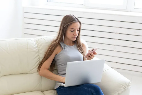 Teknik, människor och frilans koncept - ung kvinna sitter i vita soffan och chatta i laptop — Stockfoto