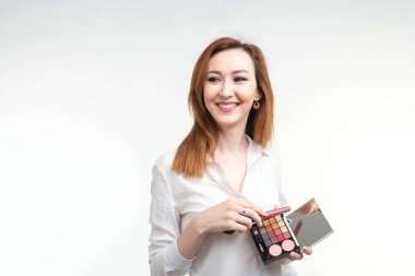 Çekici visagist veya Kore makyöz makyaj fırçaları ve bir palet göz gölge beyaz arka plan üzerinde tutan