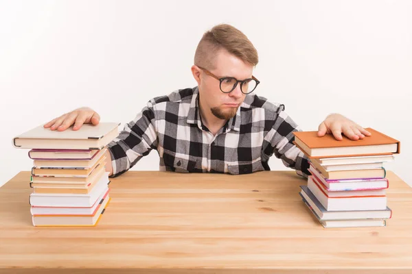 Concepto de personas, conocimiento y educación: estudiante varón cansado sentado a la mesa con montañas de libros y que no quiere estudiar — Foto de Stock