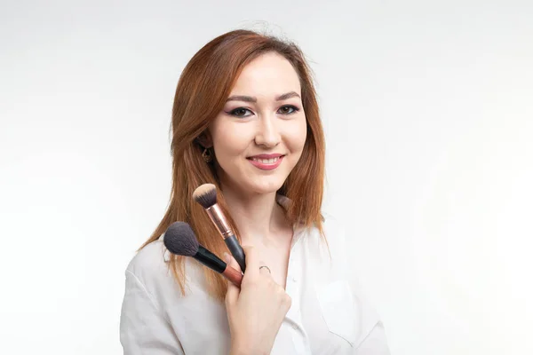 Visagistin, Schönheits- und Kosmetikkonzept - koreanische Visagistin mit Make-up-Pinseln auf weißem Hintergrund — Stockfoto