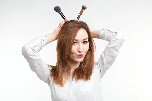 Visagistin, Schönheits- und People-Konzept - lustige koreanische junge Frau, die mit Make-up-Pinseln auf weißem Hintergrund herumalbert — Stockfoto