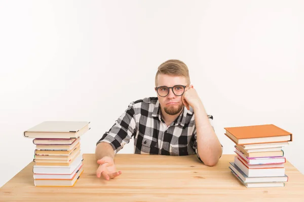 Concepto de personas, conocimiento y educación: estudiante varón cansado sentado a la mesa con montañas de libros y que no quiere estudiar — Foto de Stock