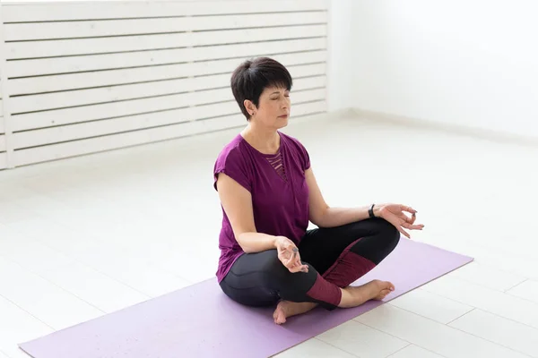 Yoga, harmony, people concept - Middle aged woman sitting in lotus position with closed eyes
