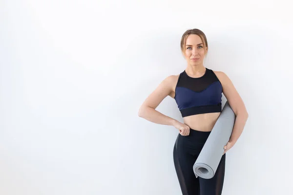 Concepto de personas, fitness y deporte - Mujer atractiva y saludable sosteniendo alfombra gris sobre fondo blanco con espacio para copiar — Foto de Stock