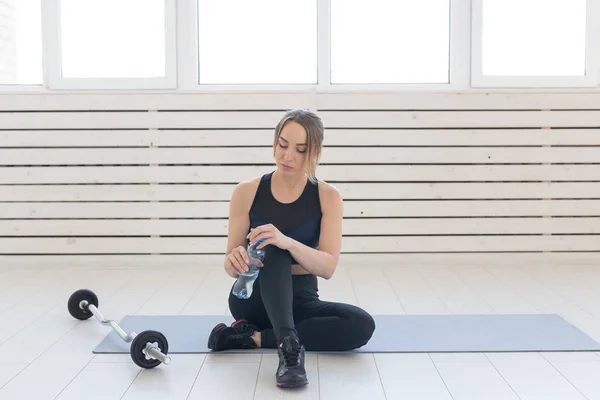 Concepto de fitness, salud y deporte: mujer joven sentada con las piernas cruzadas y bebiendo agua de la botella después del entrenamiento — Foto de Stock