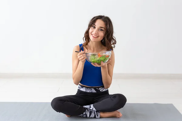 Estilo de vida saludable, personas y concepto deportivo - Mujer de yoga con un tazón de ensalada de verduras después de entrenar sobre fondo blanco — Foto de Stock