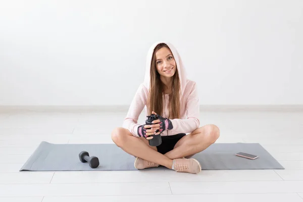 Estilo de vida saludable, personas y concepto deportivo - Mujer sentada en una esterilla de yoga y bebiendo agua después de un duro entrenamiento — Foto de Stock