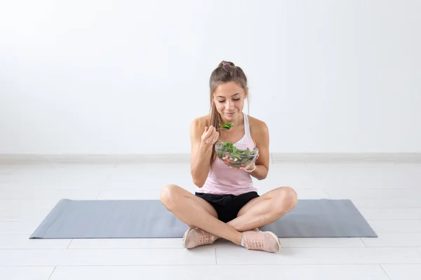 Personas, estilo de vida saludable y concepto de acondicionamiento físico - Hermosa mujer sentada en el suelo después del entrenamiento y comiendo ensalada saludable —  Fotos de Stock