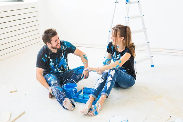 Conceito de renovação, redecoração e interiores - Jovem casal sentado no chão branco e despeje tinta e se divertindo — Fotografia de Stock