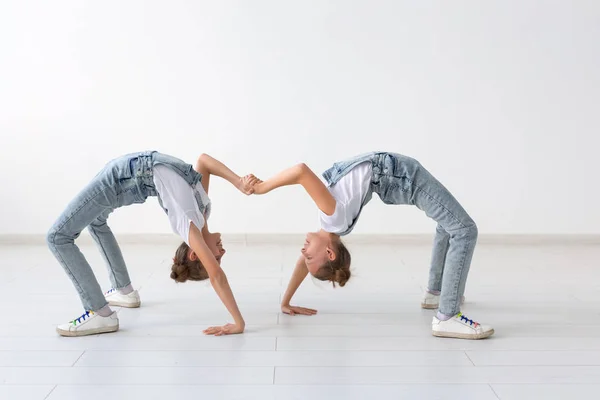 Conceito de família e esporte - Duas meninas gêmeas acrobata estão de pé nas mãos sobre fundo branco — Fotografia de Stock