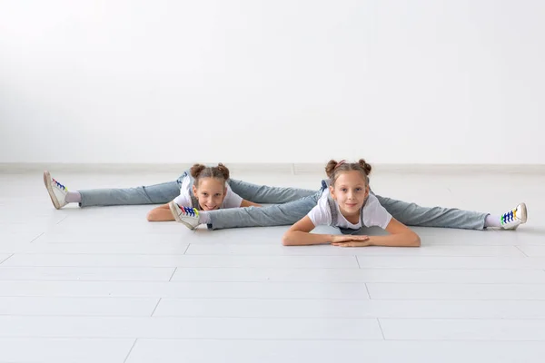 Pessoas, crianças e conceito acrobático - pequenas irmãs gêmeas fazendo exercícios em fundo branco — Fotografia de Stock