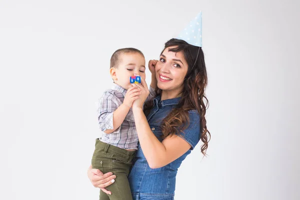 Personas, niños y concepto de vacaciones - Madre encantadora sostiene a su hijo con gorra de cumpleaños sobre fondo blanco — Foto de Stock