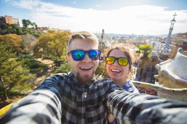 Komik genç çift kamera ile akıllı telefon Park Guell, Barselona, İspanya, gülümseyen fotoğrafı çekmek.
