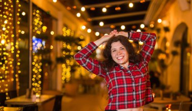 Gece hayatı, insanlar ve eğlence kavramı - güzel genç kadın sokakta parlak restoran yakınında gece poz veriyor