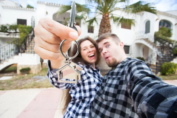 Concepto de bienes raíces y propiedades - Pareja feliz sosteniendo las llaves de un nuevo hogar y casa en miniatura —  Fotos de Stock