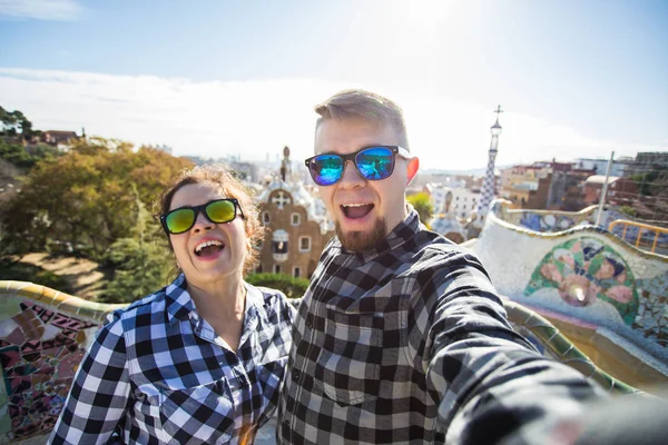 Pareja joven y divertida mirando a la cámara tomando fotos con el teléfono inteligente sonriendo en Park Guell, Barcelona, España . — Foto de Stock