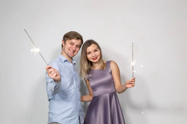 Conceito de festa, família e feriados - jovem casal olhando para faíscas no fundo branco — Fotografia de Stock