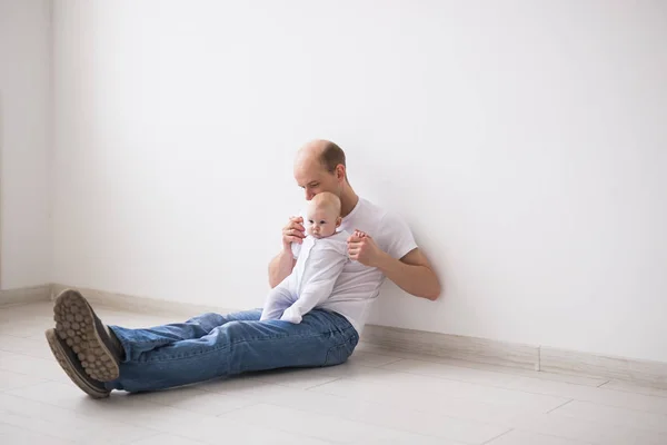 유아, 가족 및 아빠가 개념-대머리 아버지 바닥과 보류 흰색 의상 입은 그의 작은 아기에 앉아 — 스톡 사진