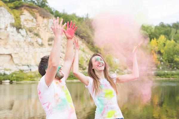 Festival holi, férias, turismo e conceito de natureza - Casal vestido com camisas brancas brincando com poeira colorida — Fotografia de Stock