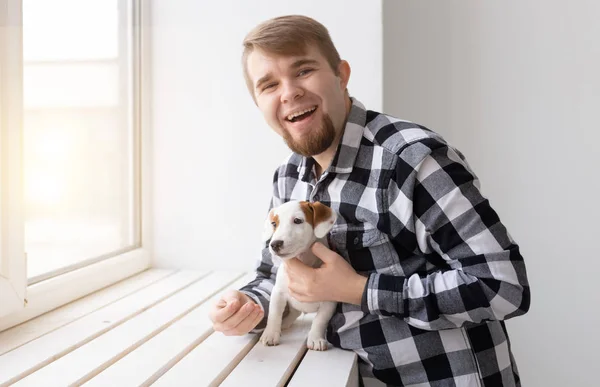 Люди, домашние животные и животные концепция - молодой человек обнимает щенка у окна на белом фоне — стоковое фото
