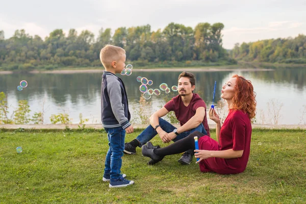 Familjen och naturen koncept - mamma, pappa och deras barn som leker med färgglada såpbubblor — Stockfoto