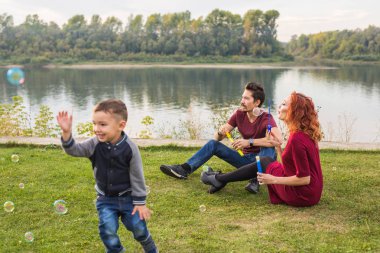 Aile ve doğa kavramı - anne, baba ve çocuklarının renkli sabun köpüğü ile oynamak