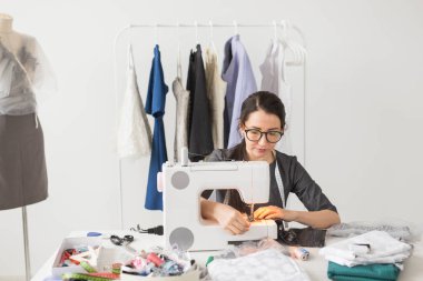 Terzi, terzi ve moda kavramı - gülümseyen kadın moda dikiş makinesi kullanarak ve onu masanın arkasında oturan Tasarımcısı