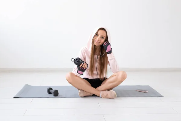 Esporte, fitness, conceito de pessoas - Uma jovem mulher fazendo uma pausa no ginásio sentado em um chão com uma garrafa de água ou bebida energética — Fotografia de Stock