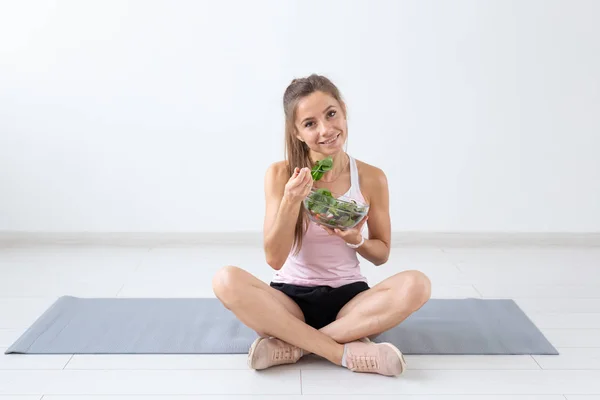 Ludzie, zdrowego stylu życia i fitness koncepcja - piękna kobieta siedzi na podłodze po treningu i jeść zdrowe sałatki — Zdjęcie stockowe