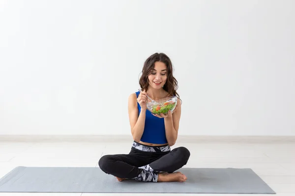 Estilo de vida saludable, personas y concepto deportivo - Mujer de yoga con un tazón de ensalada de verduras después de entrenar sobre fondo blanco — Foto de Stock