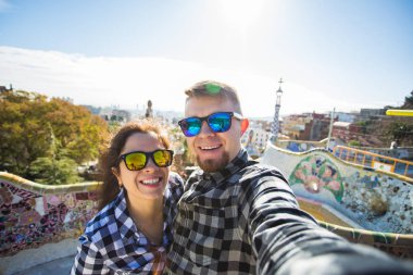 Komik genç çift kamera ile akıllı telefon Park Guell, Barselona, İspanya, gülümseyen fotoğrafı çekmek.