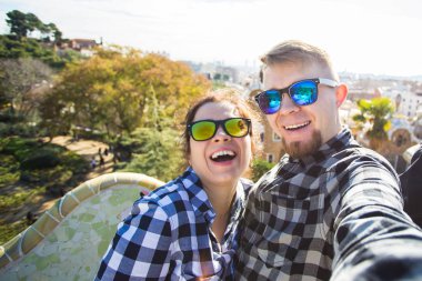 Komik genç çift kamera ile akıllı telefon Park Guell, Barselona, İspanya, gülümseyen fotoğrafı çekmek.