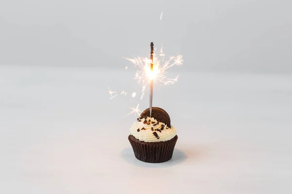 Food, holidays, happy birthday, bakery and desserts concept - delicious cupcake with sparkler on white table.