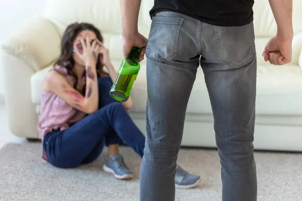 Opfer, häusliche Gewalt, Missbrauch und alkoholisches Konzept - Betrunkener Mann mit Flasche neben seiner auf dem Boden sitzenden Frau — Stockfoto