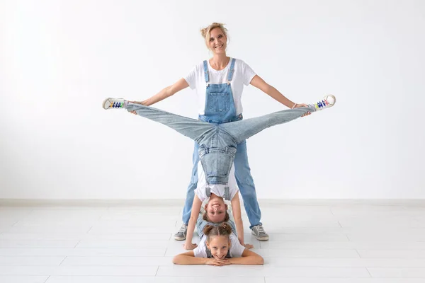 Pessoas, conceito de família e esporte - jovem mãe com gêmeos filhas fazendo exercícios em fundo branco — Fotografia de Stock