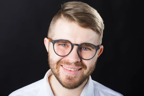 Close up retrato de homem barbudo bonito sorridente em óculos elegantes em pé contra a parede preta — Fotografia de Stock