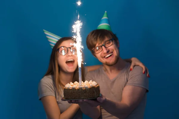 Komik nerd adam ve kadın tatil kapaklar ve gözlük mavi arka plan üzerinde mumlar ile doğum günü pastası tutan giyiyor — Stok fotoğraf