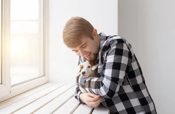 사람, 애완 동물 및 개 개념-창 배경 위에 젊은 남자 지주 강아지 잭 러셀 테리어 — 스톡 사진