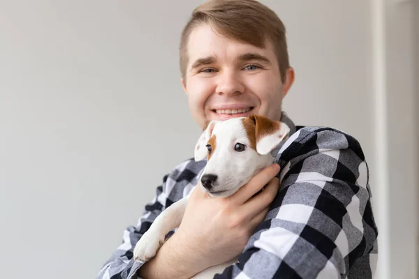 people, pets and animals concept - close up of young man hugging jack russell terrier puppy on white background