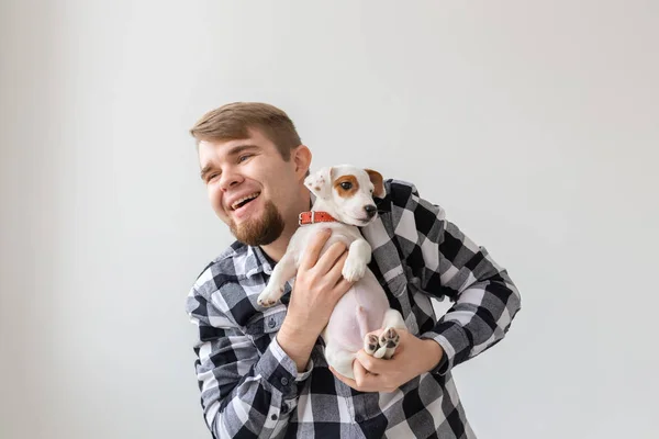 people, pets and animals concept - handsome man holding jack russell terrier puppy on white background