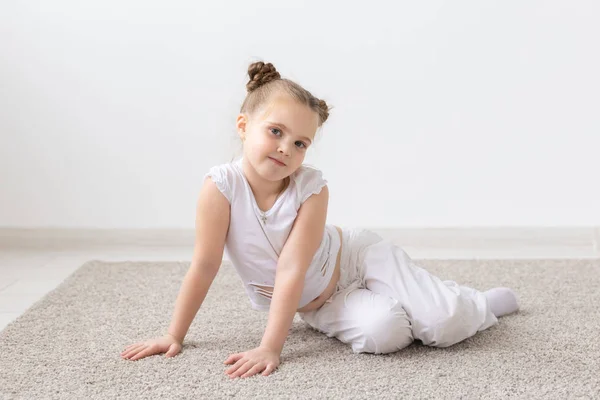 Barn och kids concept - litet barn flicka klädd i vit skjorta sitter på golvet med vackert ansikte — Stockfoto