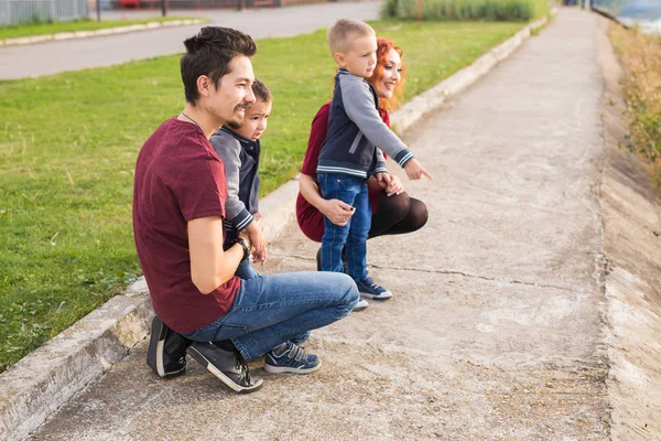 La paternidad, la infancia y el concepto familiar - Padres y dos niños varones caminando por el parque y mirando algo — Foto de Stock