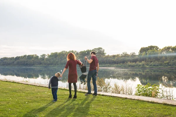 Parenthood and nature concept -Family of mother and father with two boys twins kids in a park at summer by a river at sunny day — Stock Photo, Image