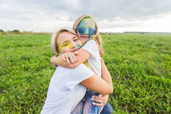 Felicidad, festival Holi y el concepto de vacaciones - Madre y su hija cubierta de polvo de color sonriendo sobre el fondo de la naturaleza —  Fotos de Stock